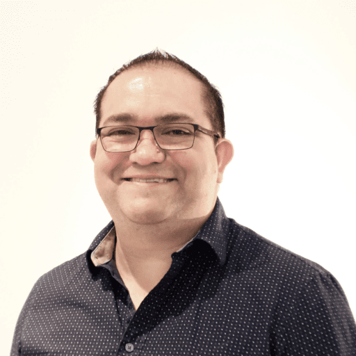 Portrait of a person with greying curly hair and dark-rimmed glasses in a dark shirt