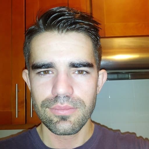 Portrait of a person with dark hair and light stubble in a plum t-shirt