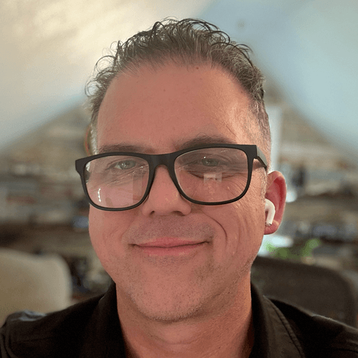 Portrait of a smiling person in glasses and a navy patterned shirt against a white backdrop